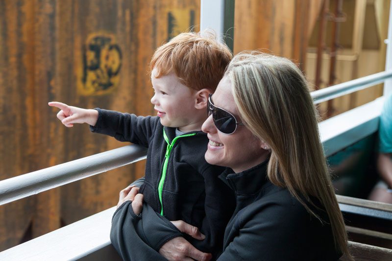 Woman holds little buy as he points and looks out from roof of train